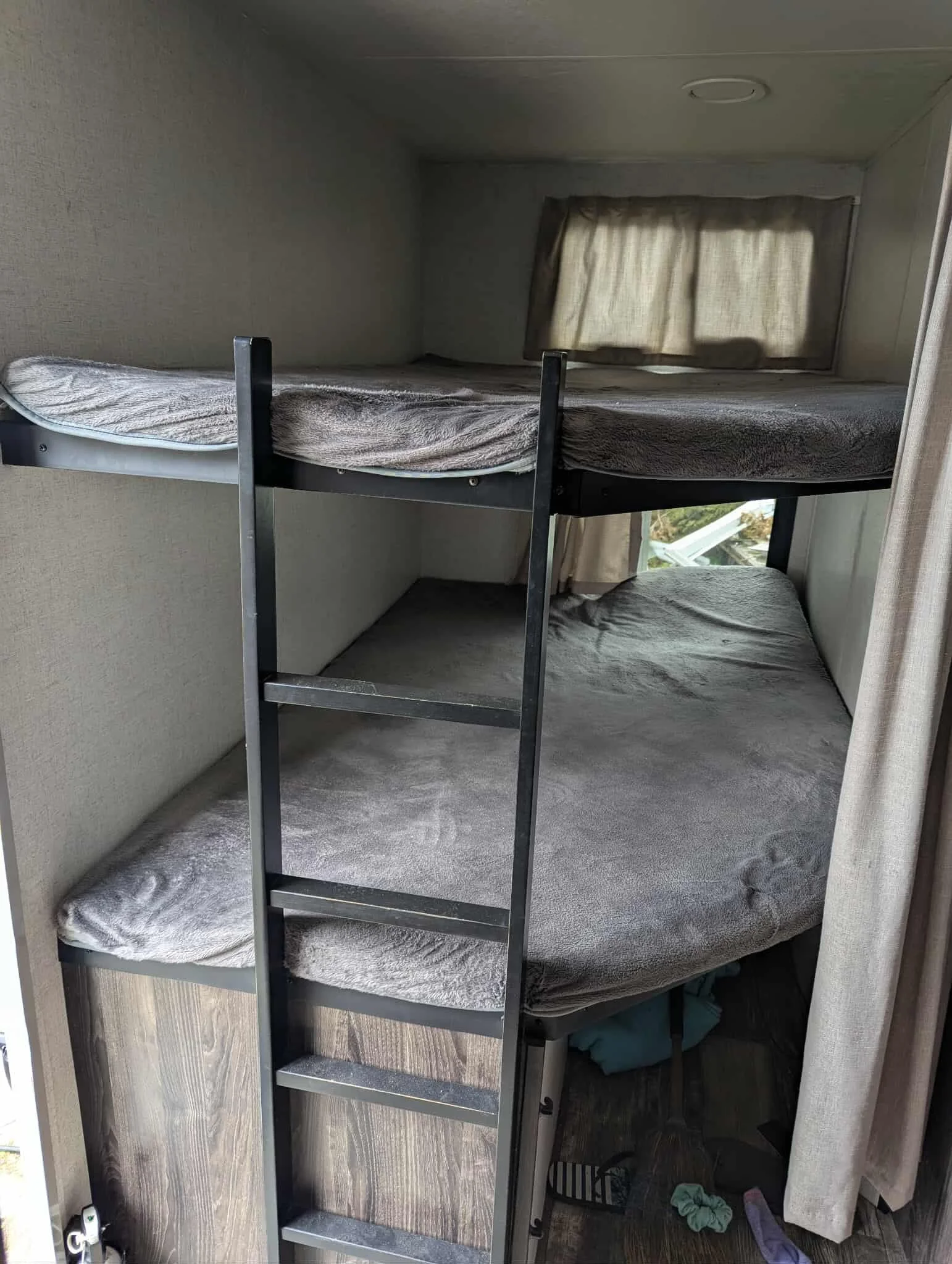 Bunk beds with gray bedding and a window with beige curtains in a small room.