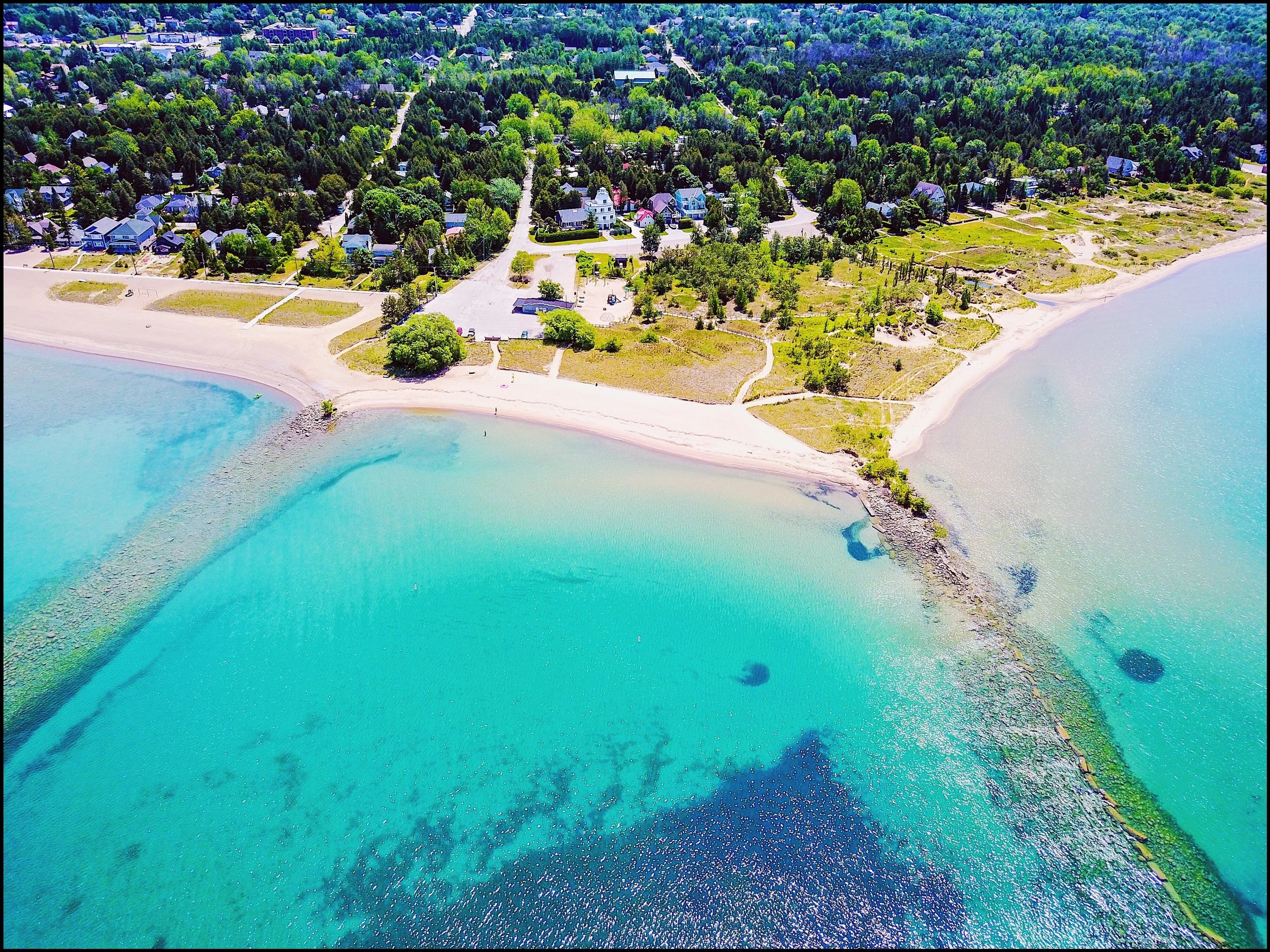 Aerial view of a coastal town with colorful houses, sandy beaches, and turquoise waters surrounded by lush greenery and trees.