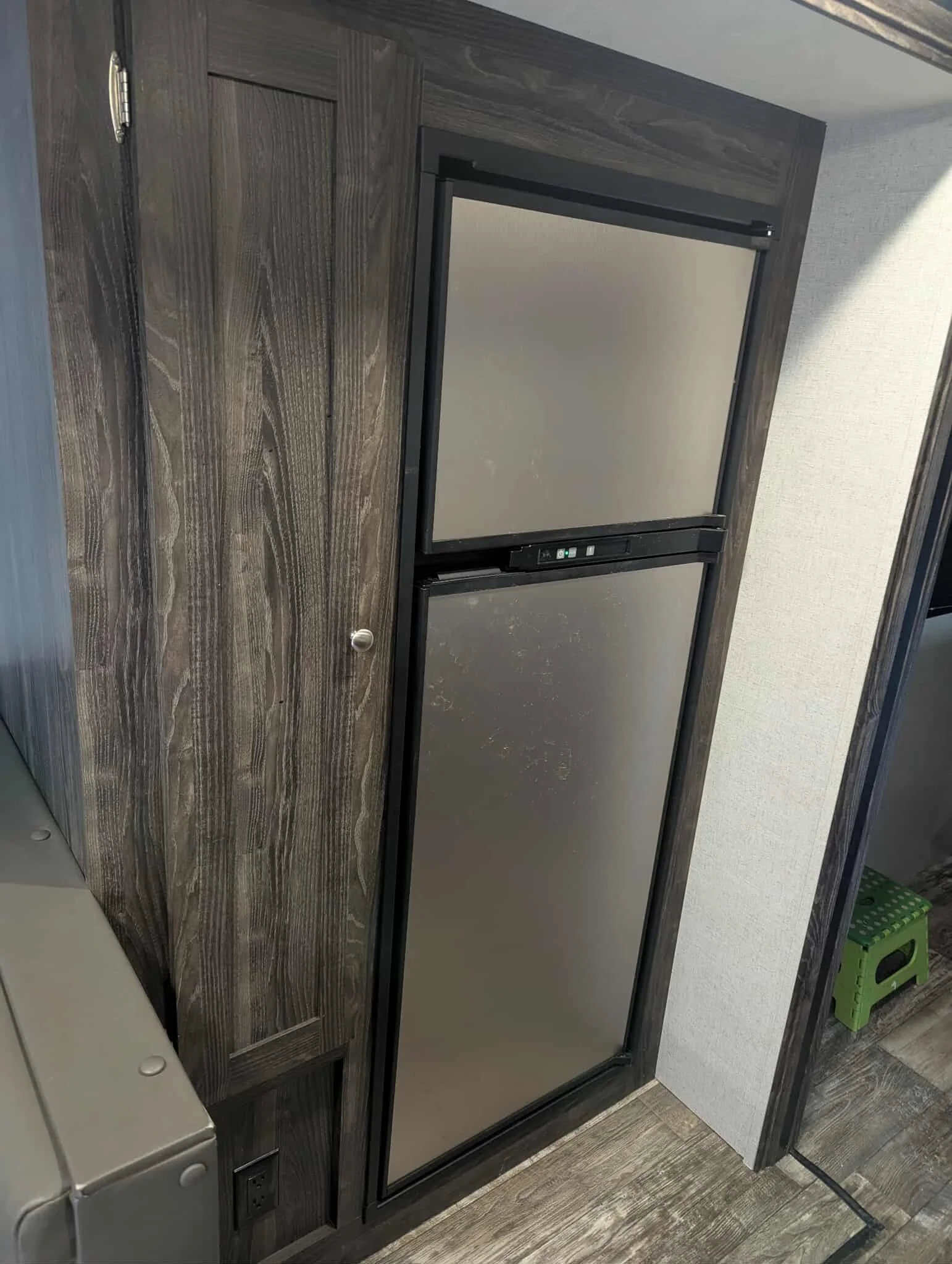A refrigerator with a dark wood finish in a room with gray floors and a white wall.