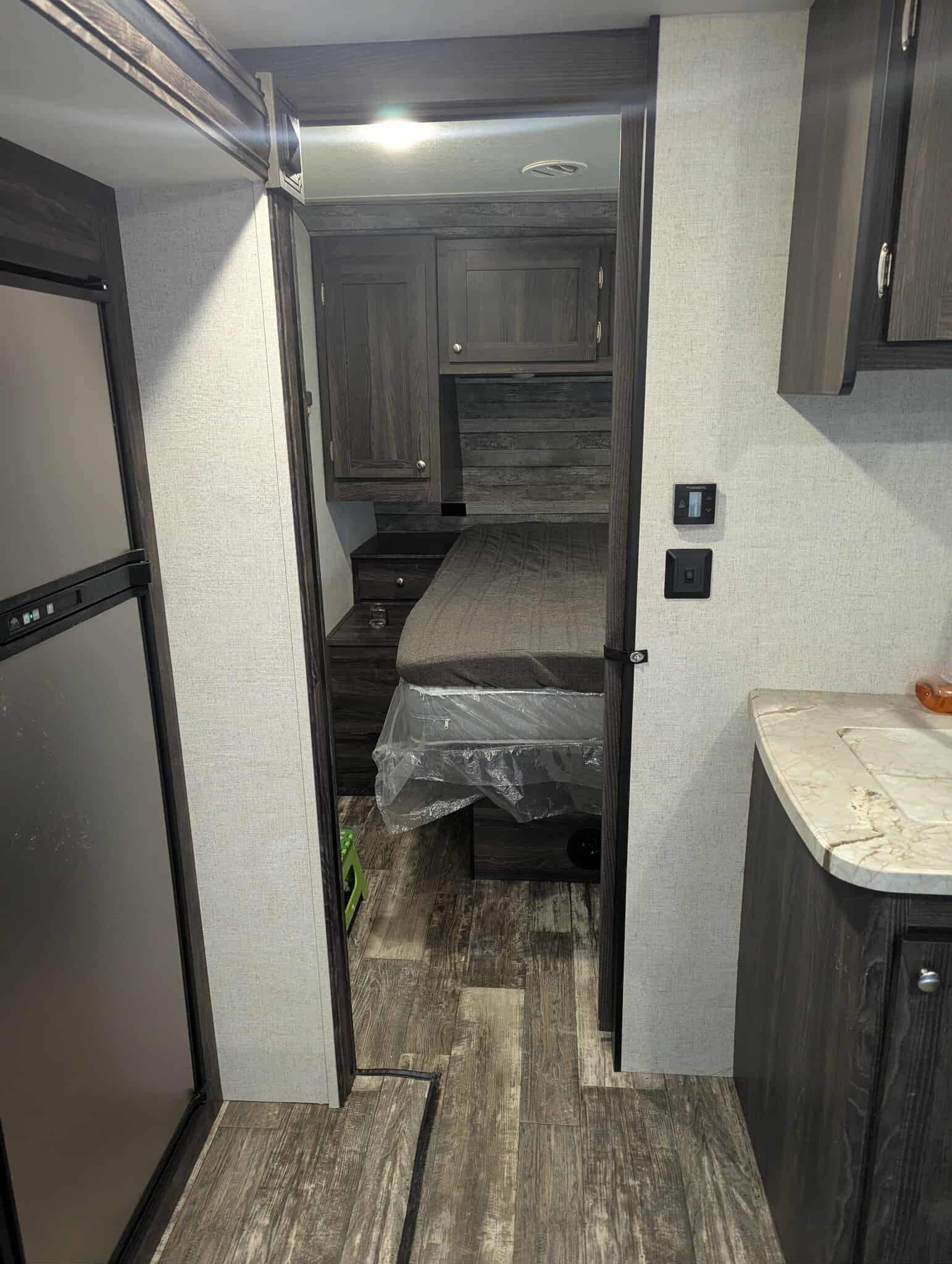 Interior of a small room with wooden cabinetry, a bed with plastic covering, and a marble countertop on the right, in an RV or camper.