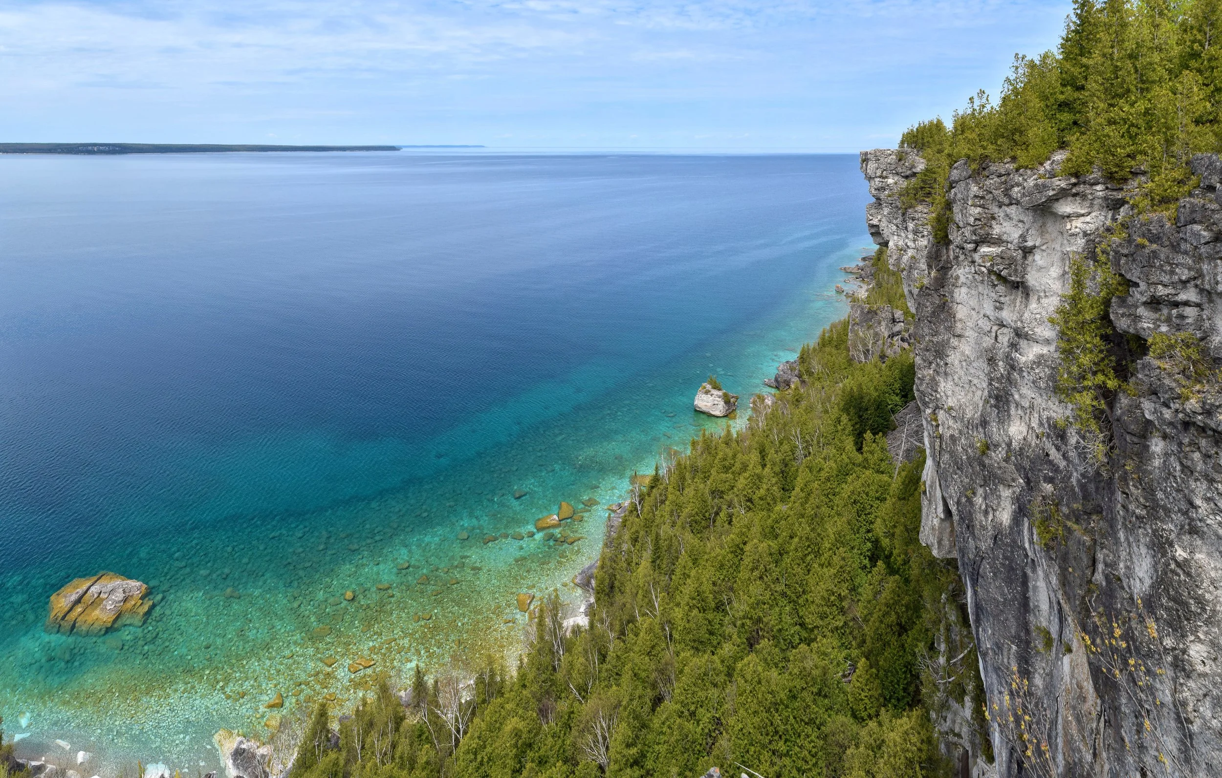Cliffside overlooking a calm blue lake with clear water and a forested shoreline in the distance.