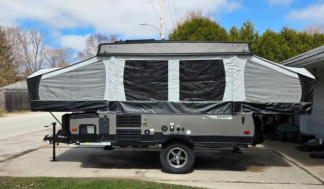 A pop-up camper trailer with extended fabric tent sides parked on a driveway during daytime.