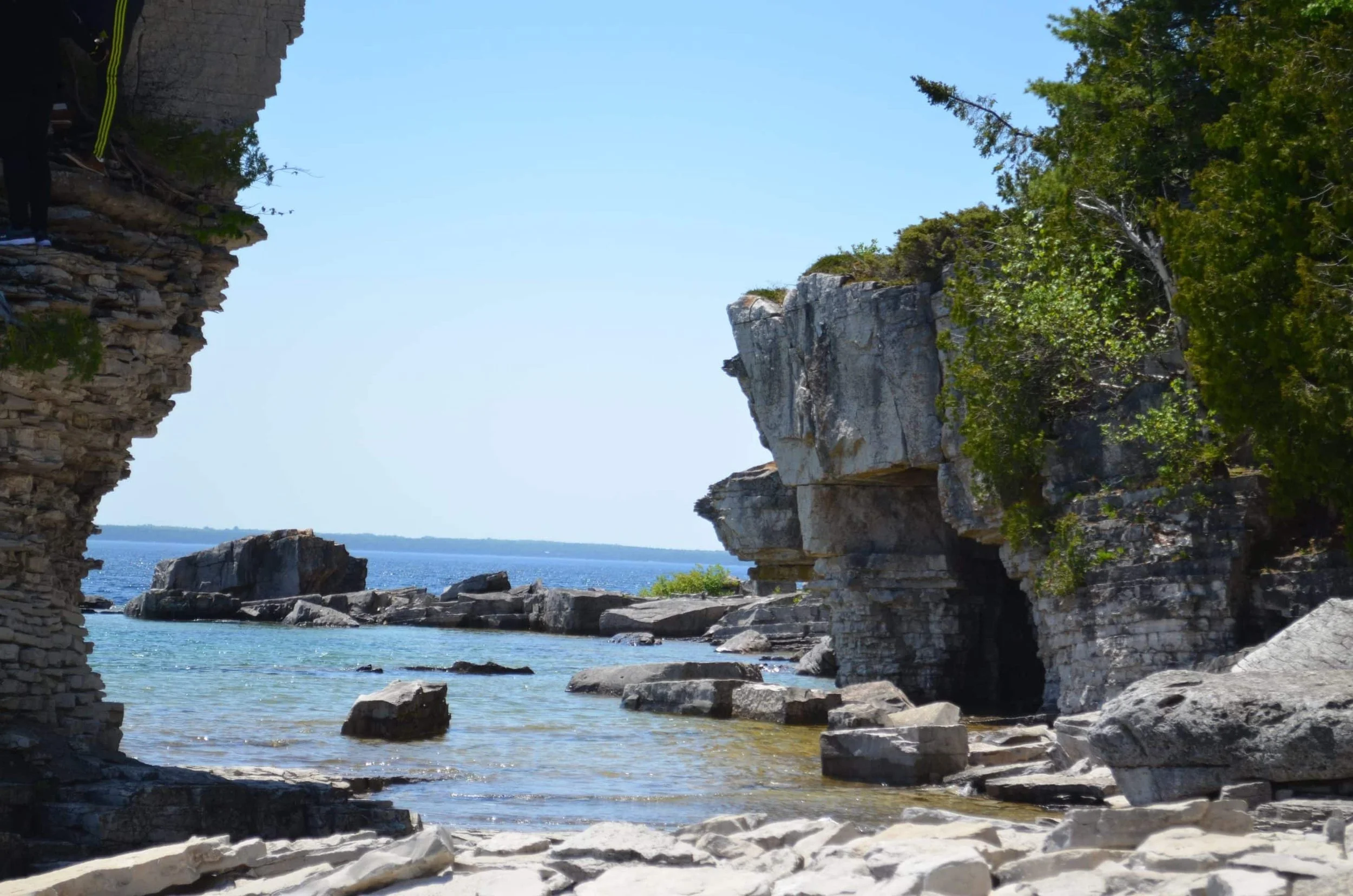 View of a rocky coastline with trees and ocean, seen from a cave or rock opening.