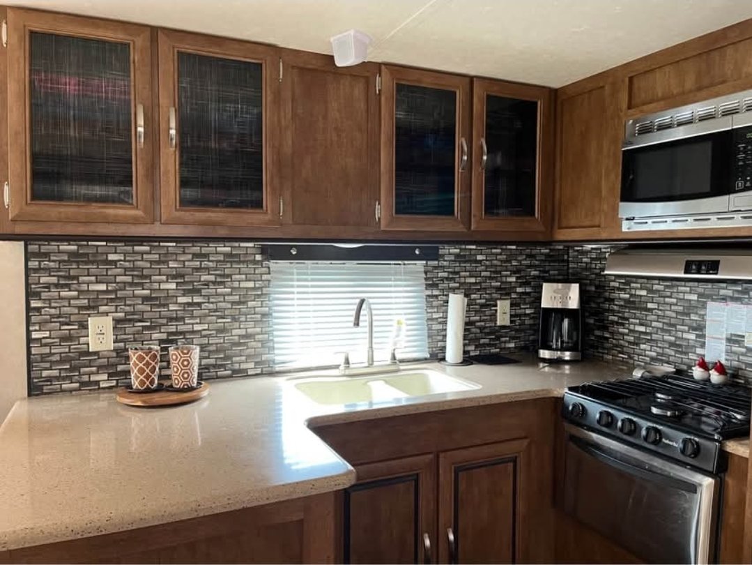 Kitchen with wooden cabinets, a black brick backsplash, a window with blinds above the sink, a coffee maker, a microwave, and a stove.