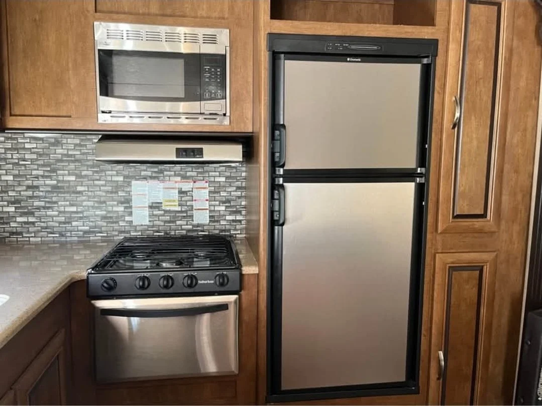 Kitchen with wooden cabinets, stainless steel refrigerator, microwave, oven, and backsplash.