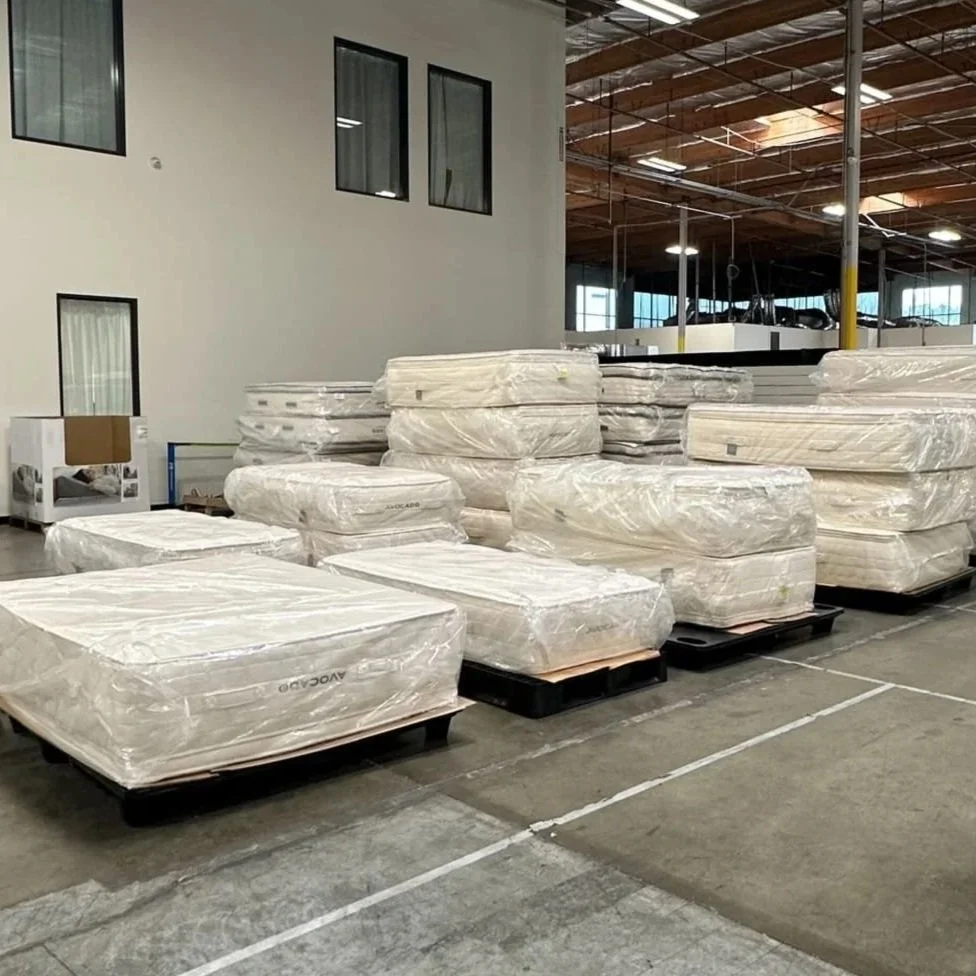 Stacks of mattresses wrapped in plastic on pallets inside a warehouse.