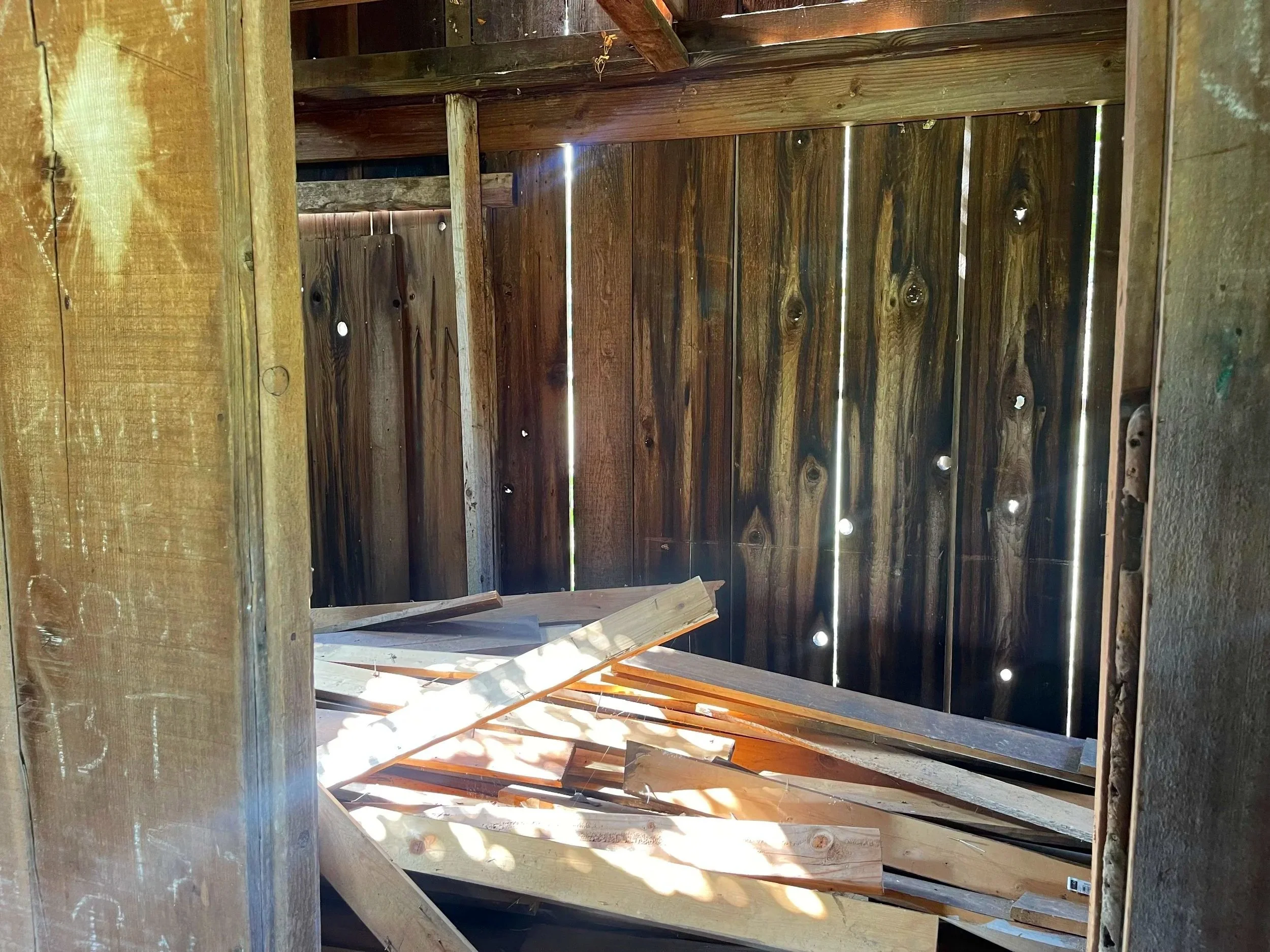 The inside view of a wooden shed with walls made of vertical wooden planks and an unfinished wooden floor.