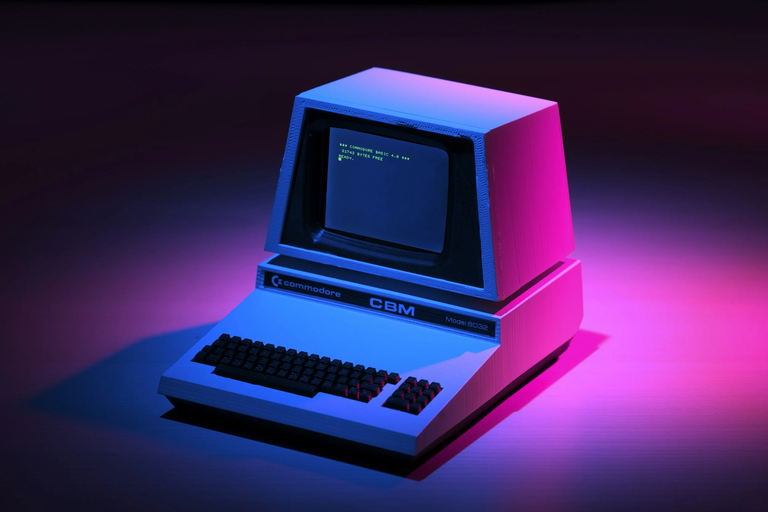Vintage Commodore 64 computer with keyboard, monitor displaying green text, illuminated by pink and blue neon lights.