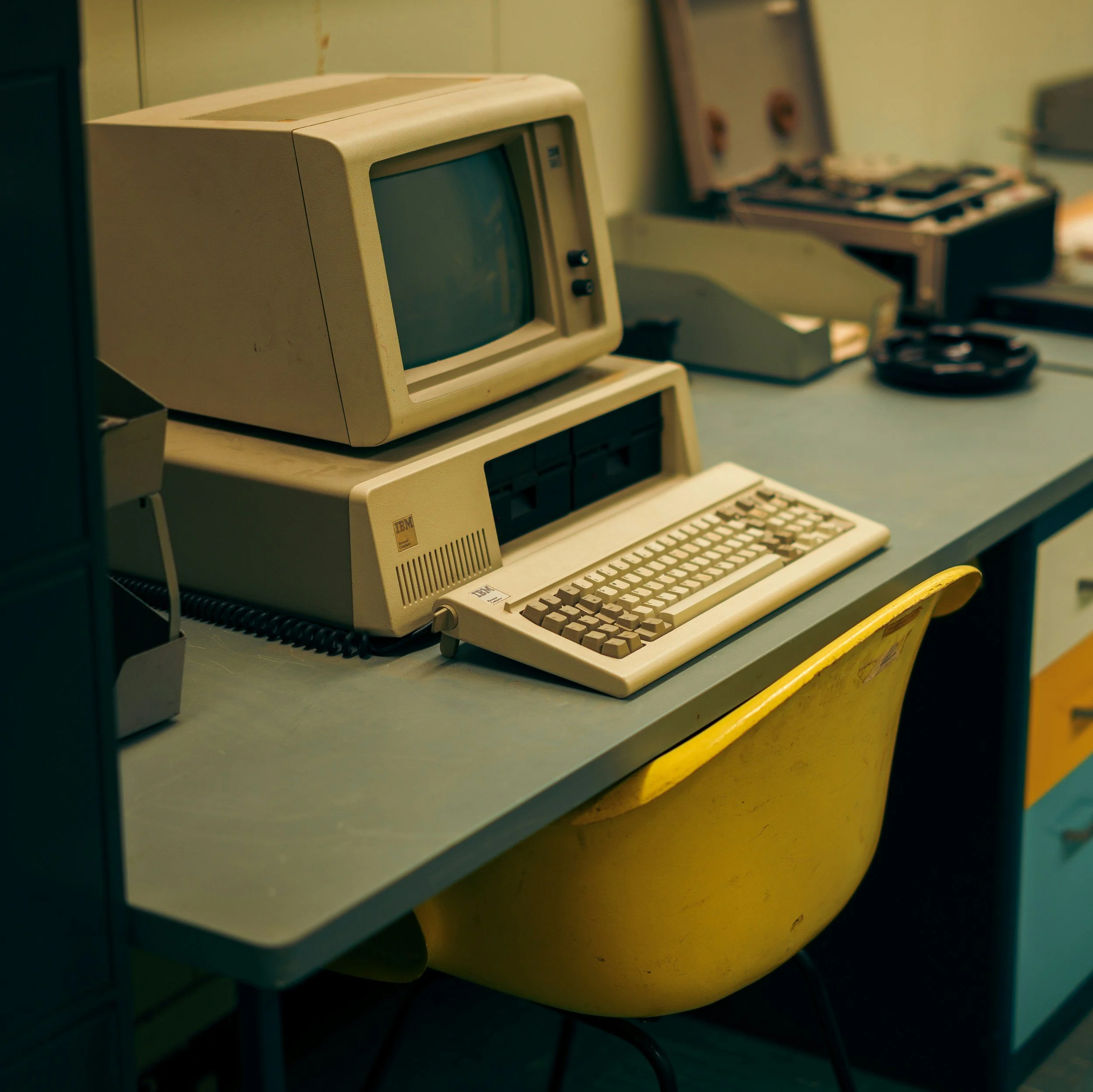 An old beige computer with a CRT monitor, keyboard, and a separate mouse resting on a yellow table.
