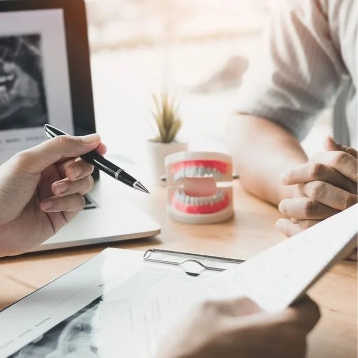 Person holding a pen and pointing towards a dental model on a desk in a consultation setting.
