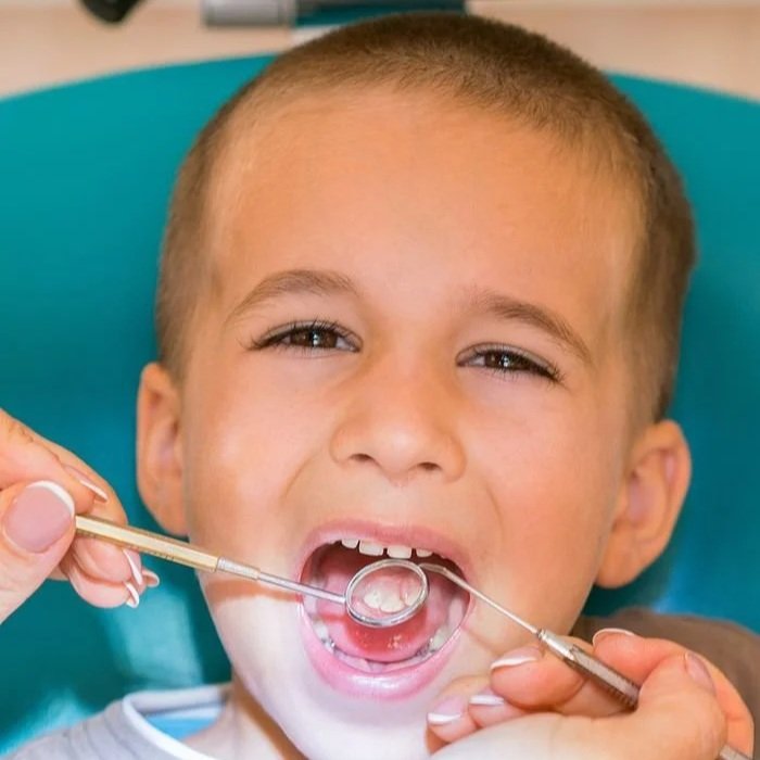 Young boy at the dentist with mouth open, dentist using dental tools.