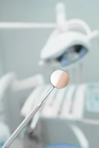 A dental mirror held in front of a dental chair and equipment in a dental clinic.