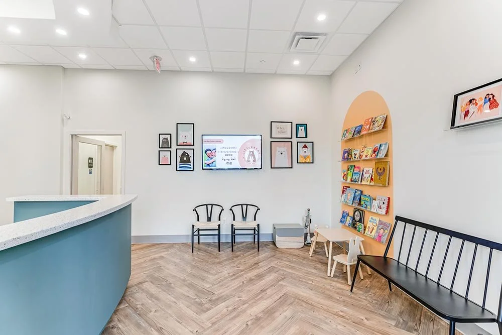 Waiting area in a children's library with bookshelves, chairs, a bench, and artwork on the wall.