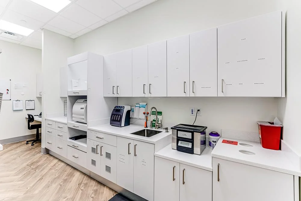 Dental office kitchenette with white cabinets, a sink, and dental equipment on the countertop.