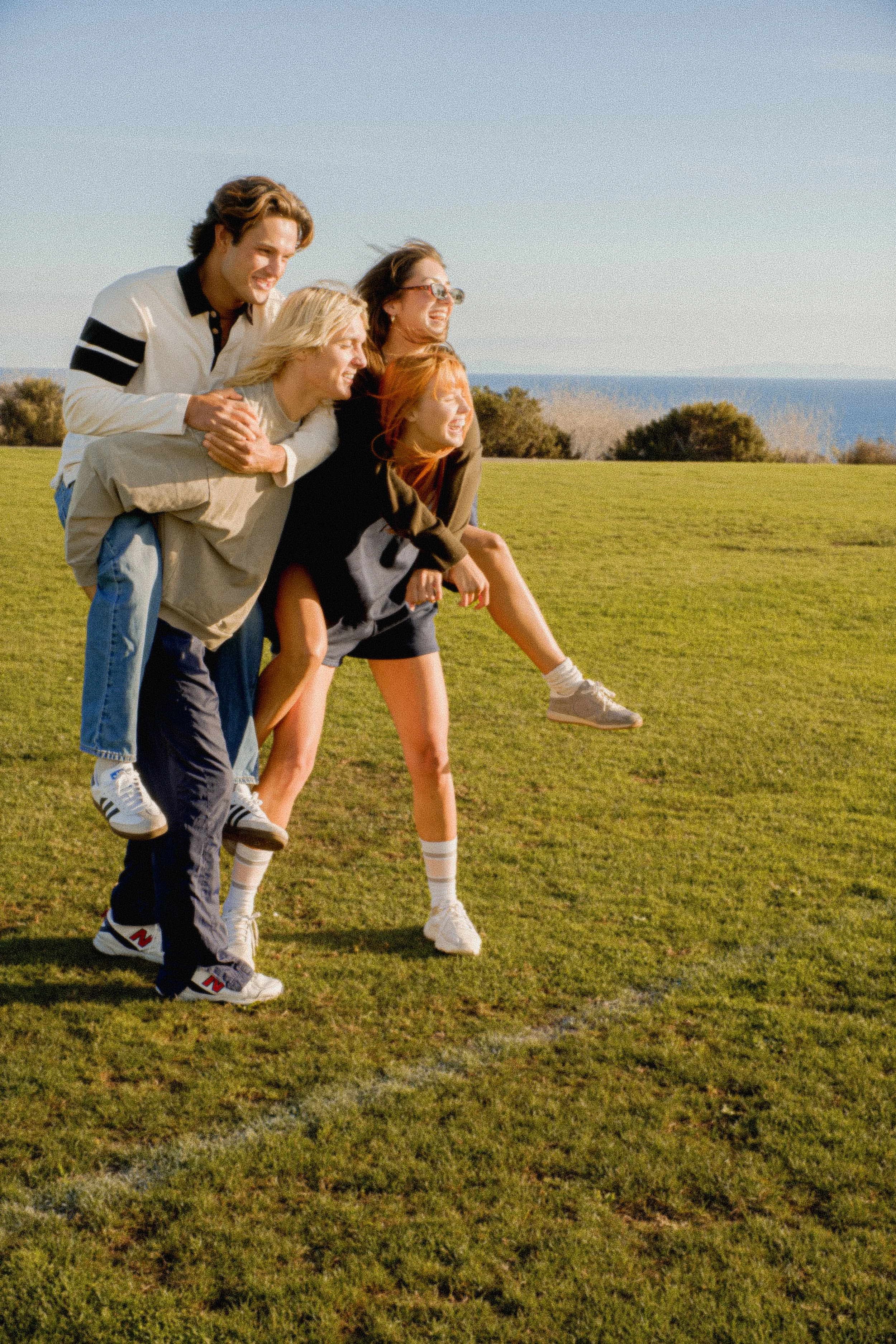 Five friends playing and laughing outdoors on a grassy field on a clear day.