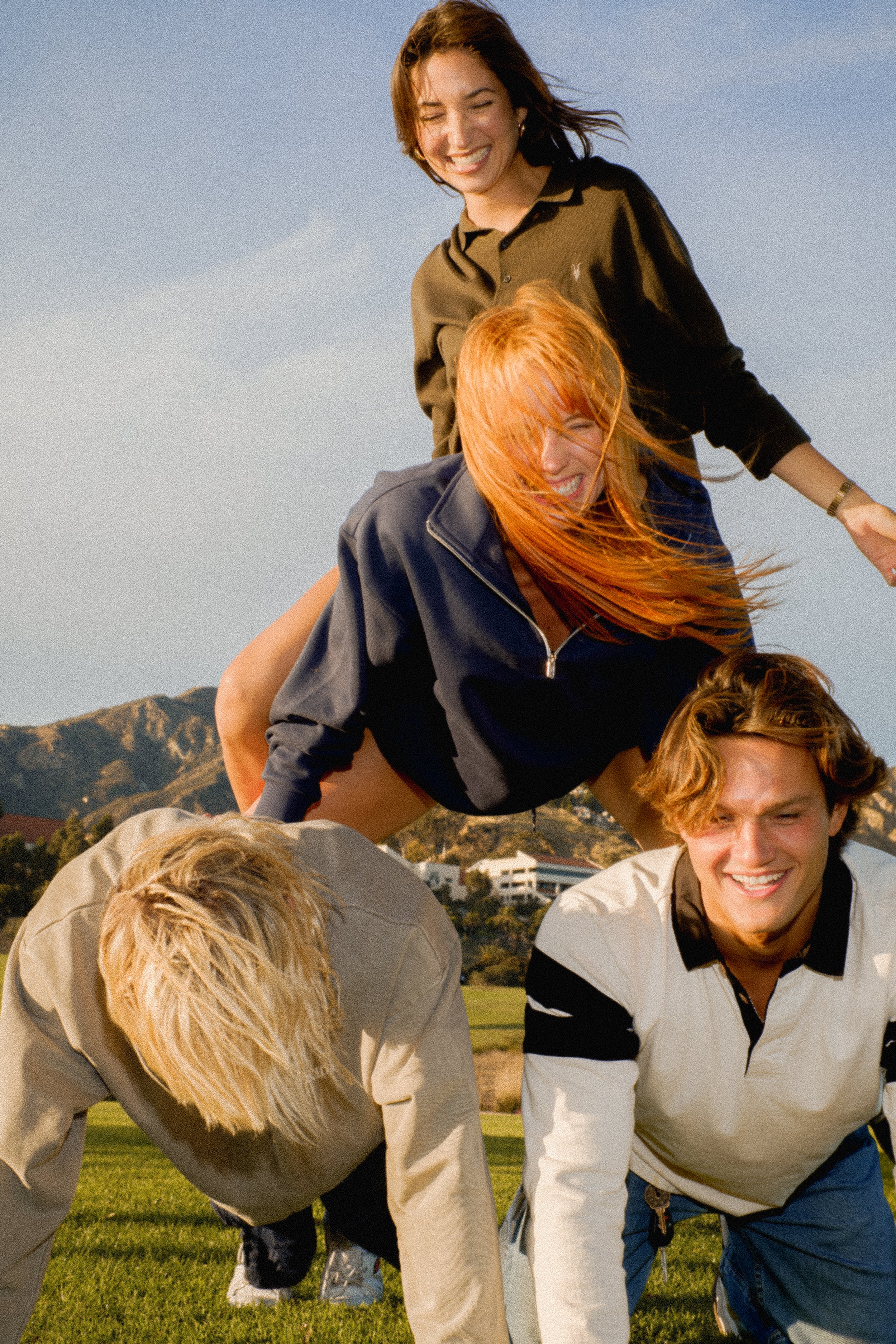 Group of young people participating in a human pyramid on a grassy field with mountains in the background