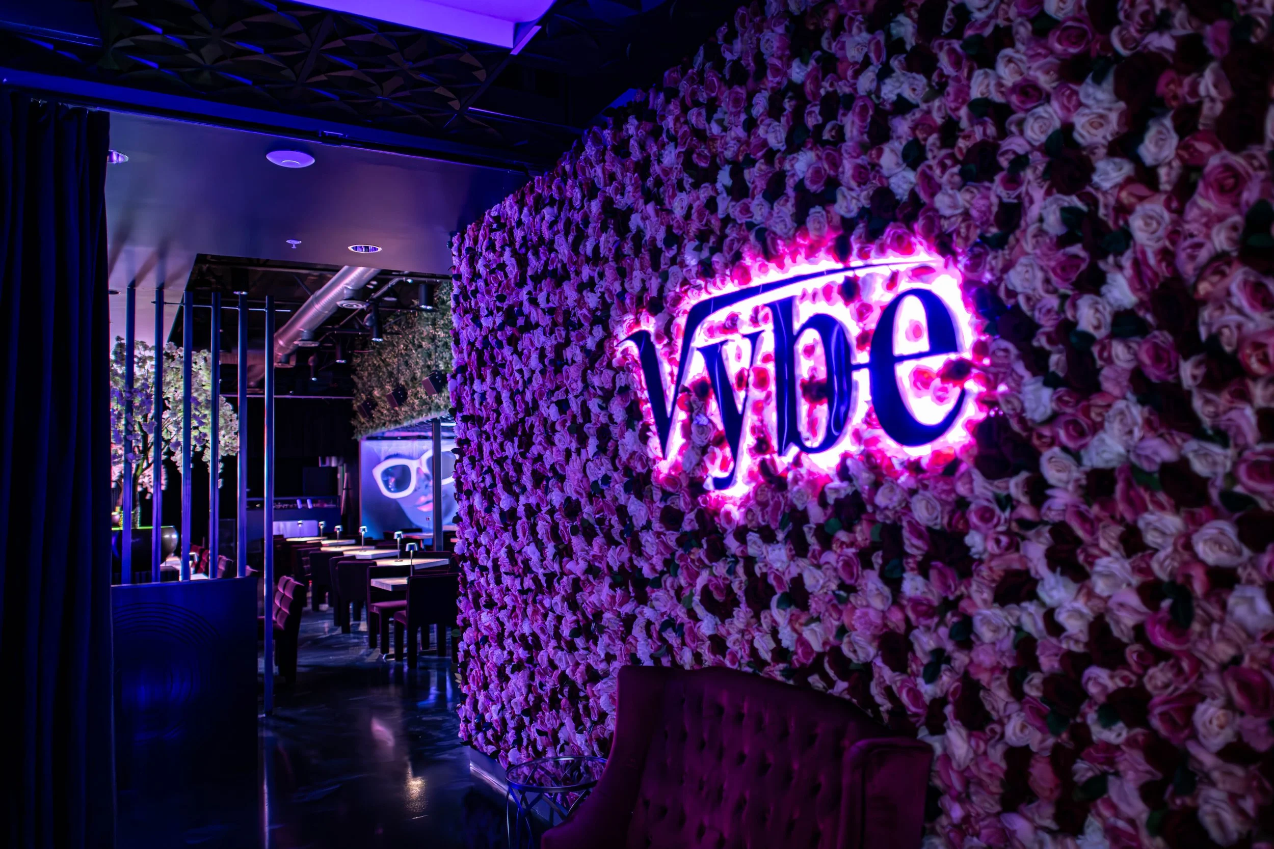 Interior of a modern venue decorated with a large wall of pink and white roses, with neon lighting spelling 'Vybe'.