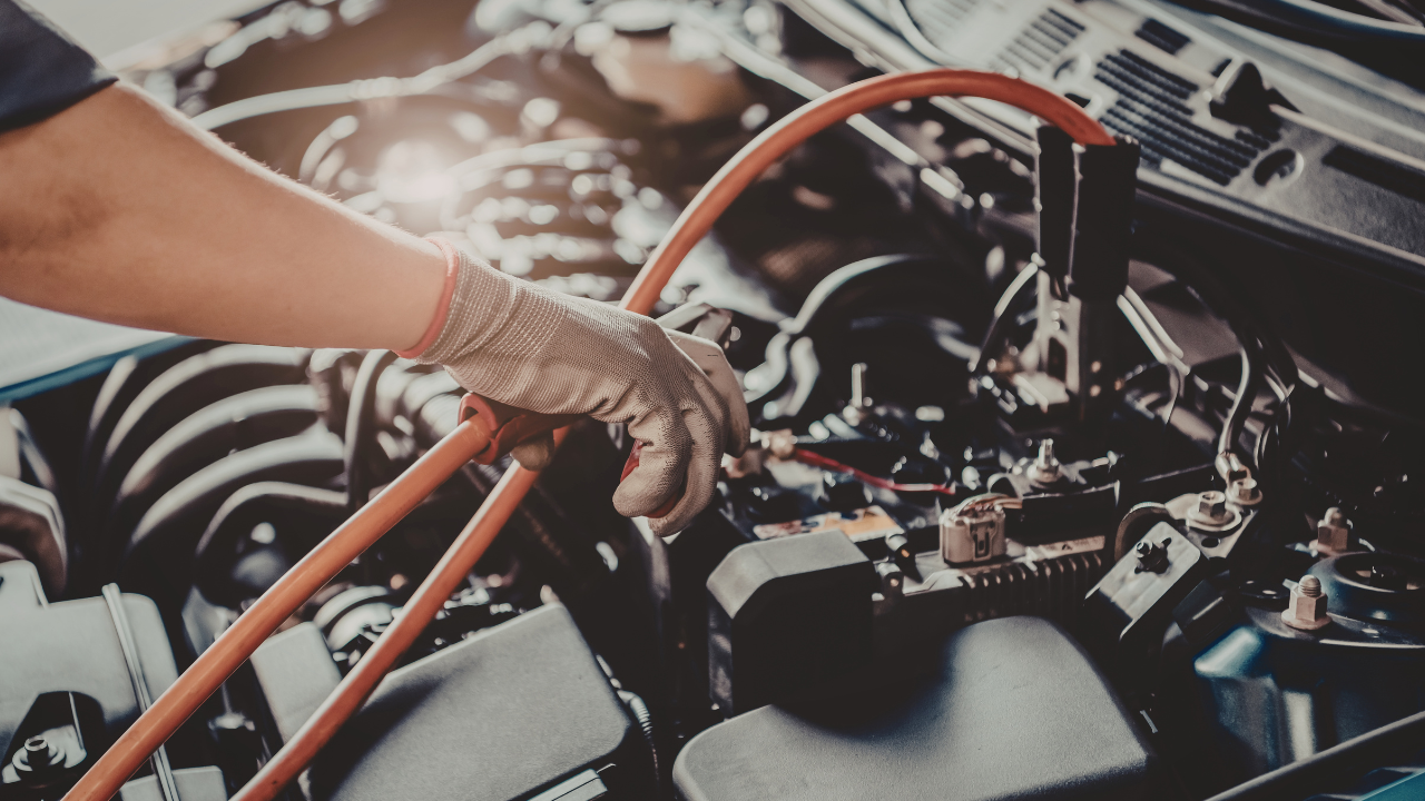 A mechanic wearing gloves working on a car engine with various parts and wires visible.