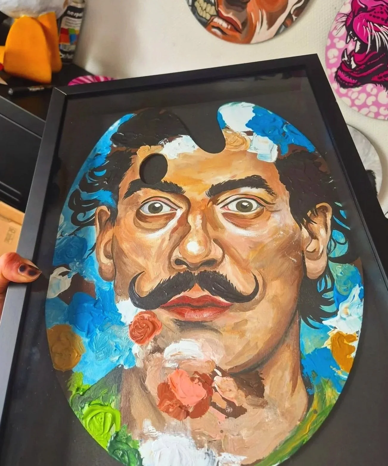 Un portrait peint de Frida Kahlo avec des couleurs vives, encadré dans un cadre noir.
