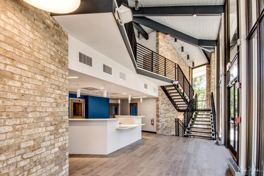 Modern lobby interior with brick walls, staircase, large windows, and a white reception desk.