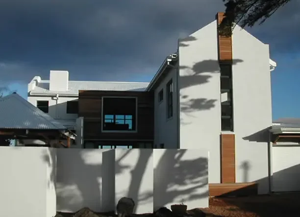 Modern white and dark wood contemporary house with a tall facade, courtyard wall, and tree shadows