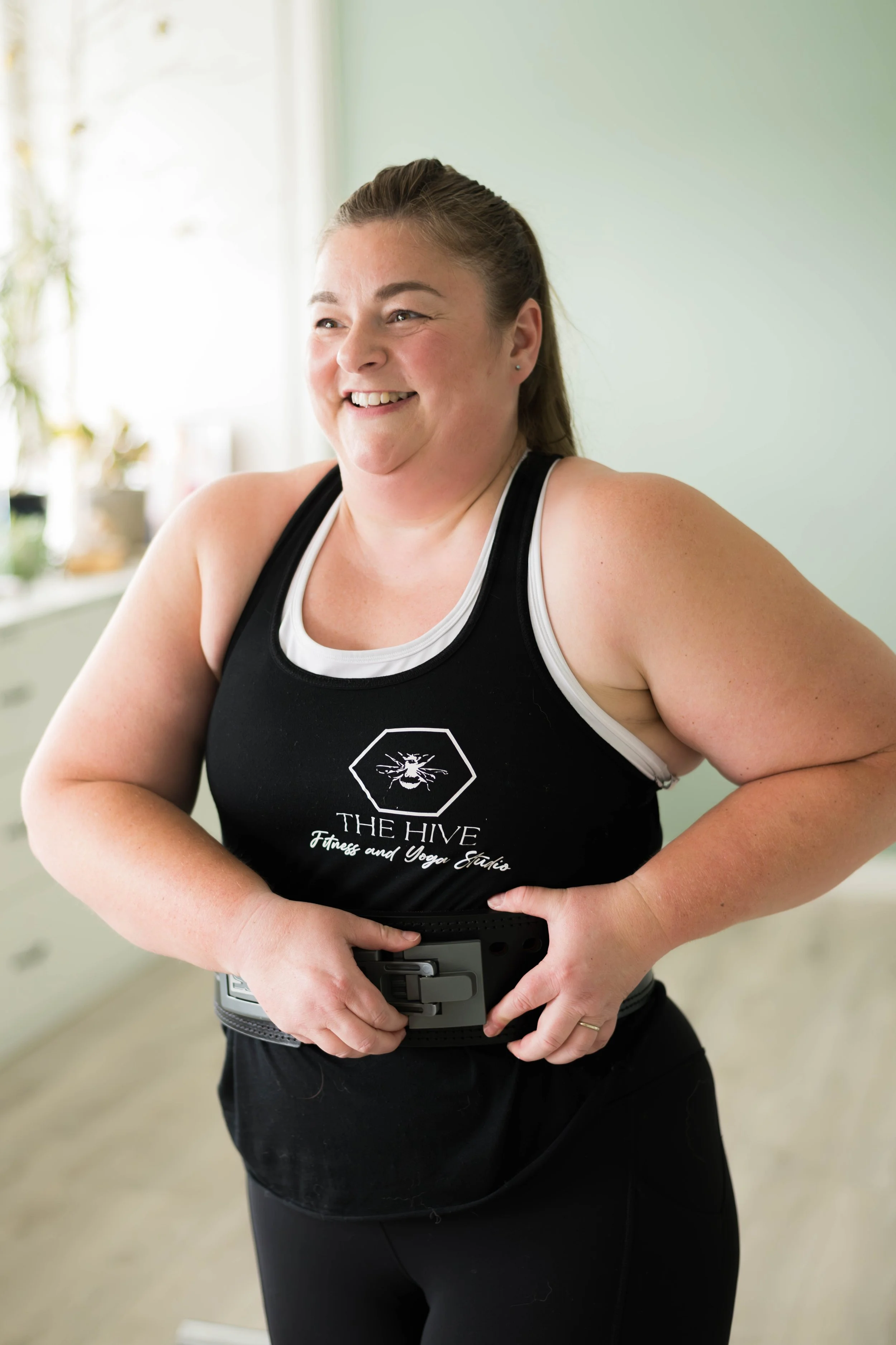 Laura smiling in The hive Fitness and Yoga Studio while adjusting weightlifting  belt