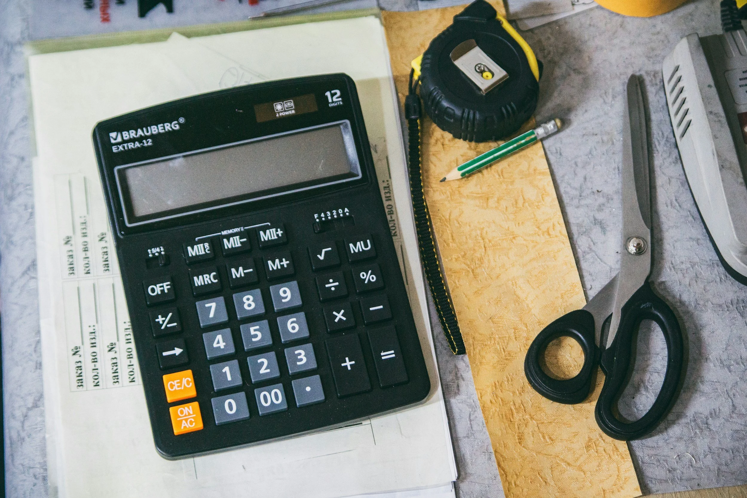 A calculator with a large display, a pencil, a tape measure, and scissors on a desk.