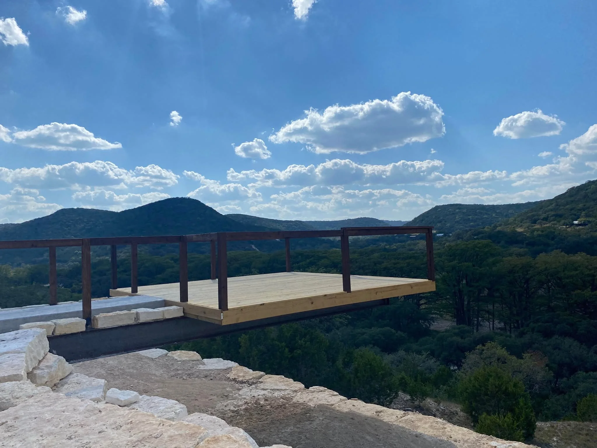 A wooden deck under construction with a scenic mountain view and a blue sky with clouds in the background.
