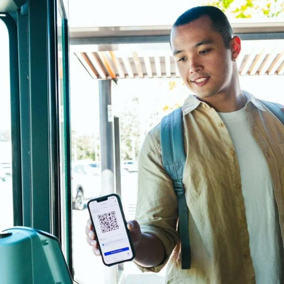 A young man with a backpack showing a phone screen with a QR code at a door scanner.