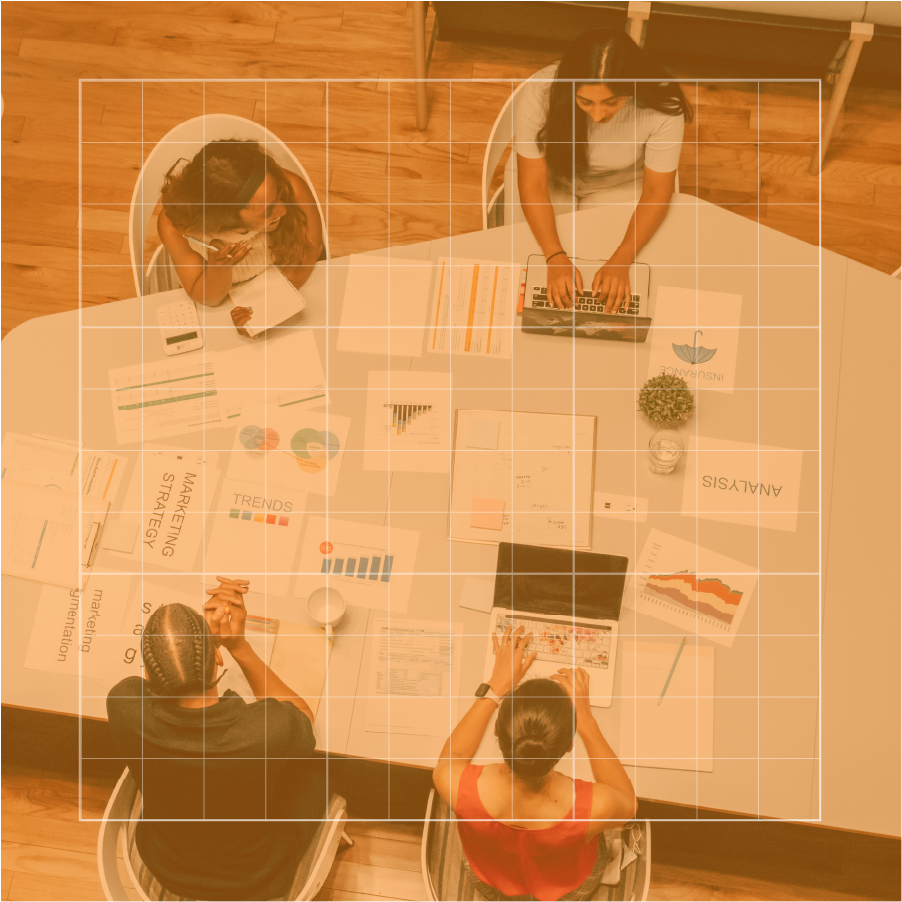Top-down view of four women in a business meeting around a white table with documents, charts, a laptop, and a calculator.