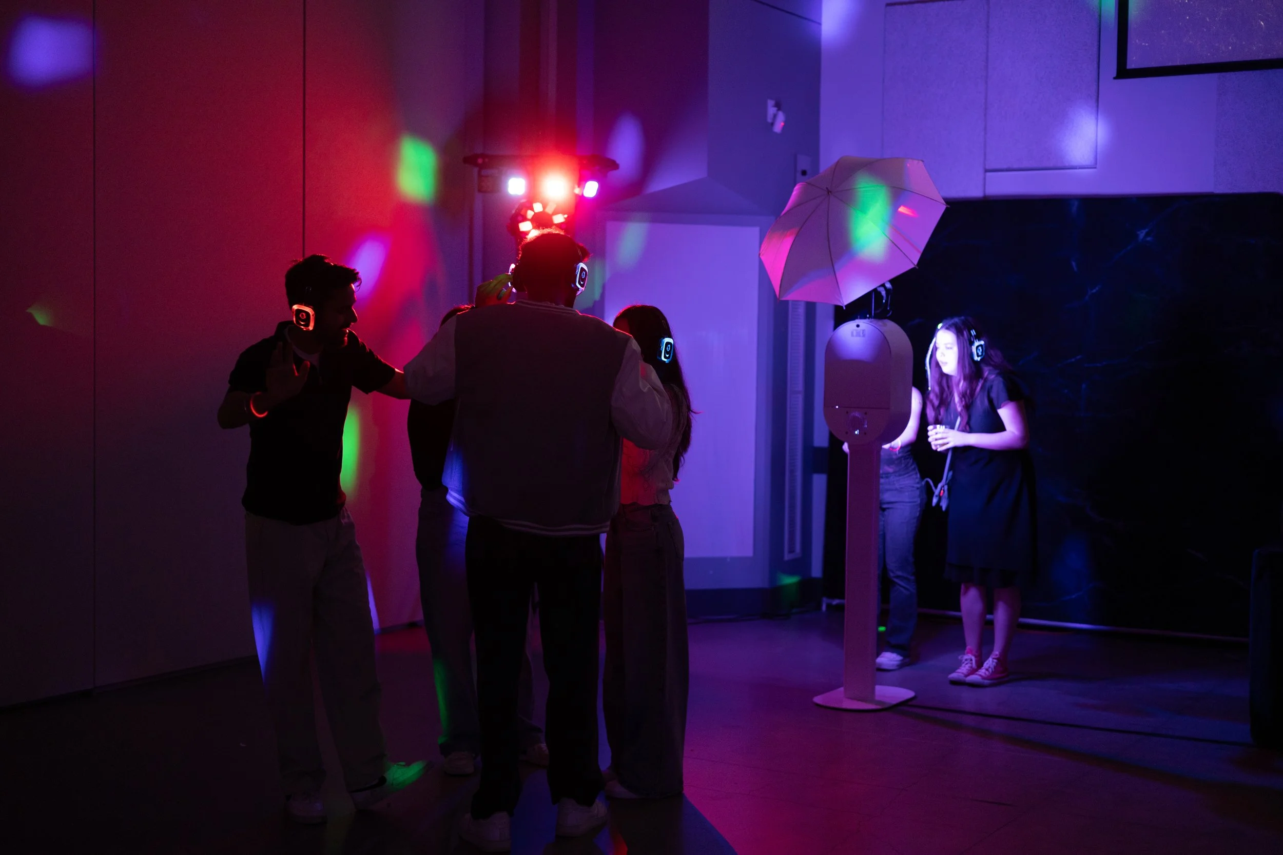 People dancing and socializing in a dark room with colorful lights and a disco ball.