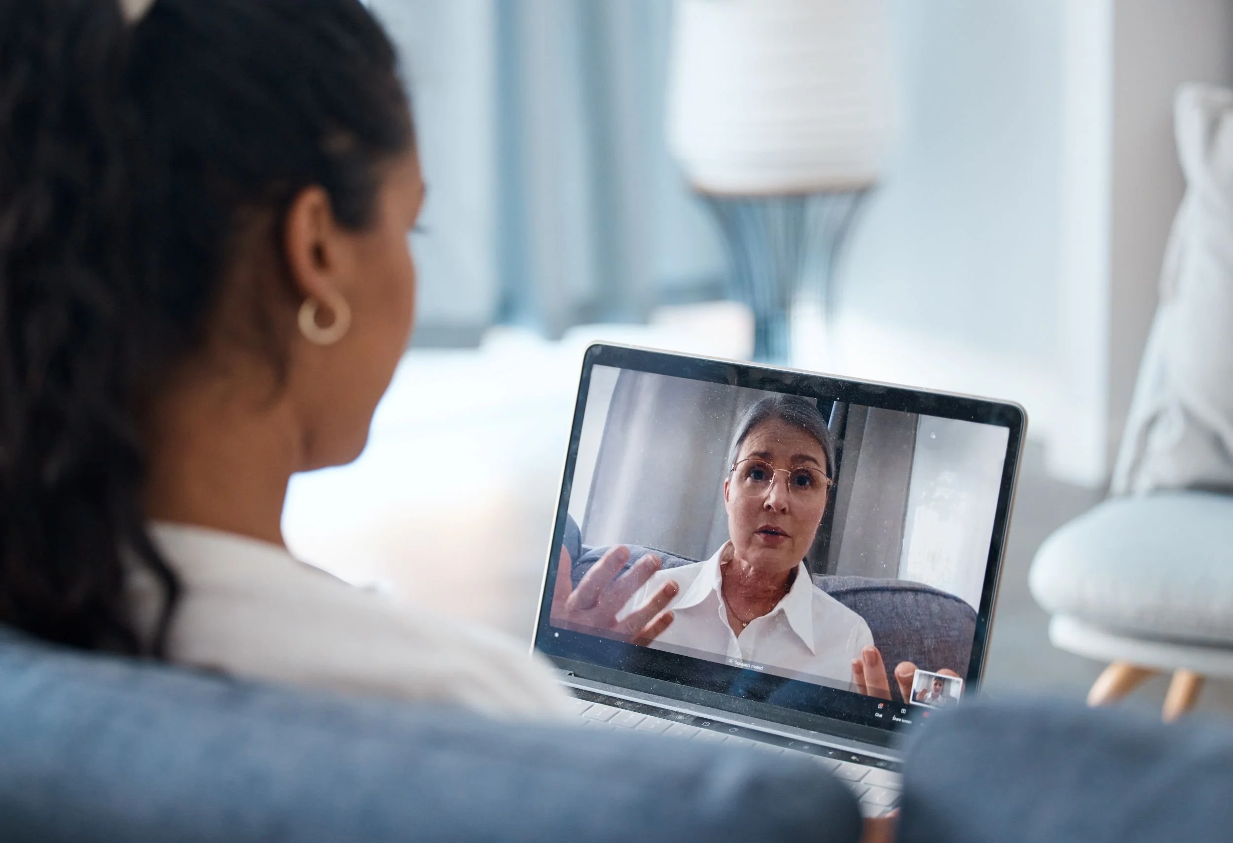 A woman is on a video call on her laptop, looking at a woman on the screen who appears to be speaking and gesturing with her hands.