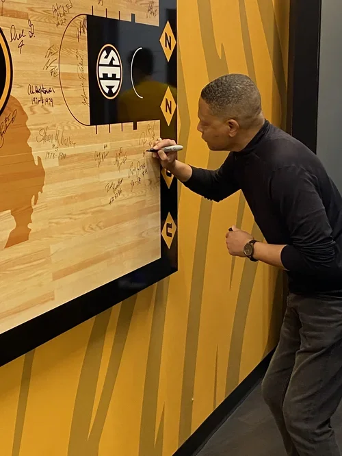 Man signing a large wooden wall with a Seahawks logo.