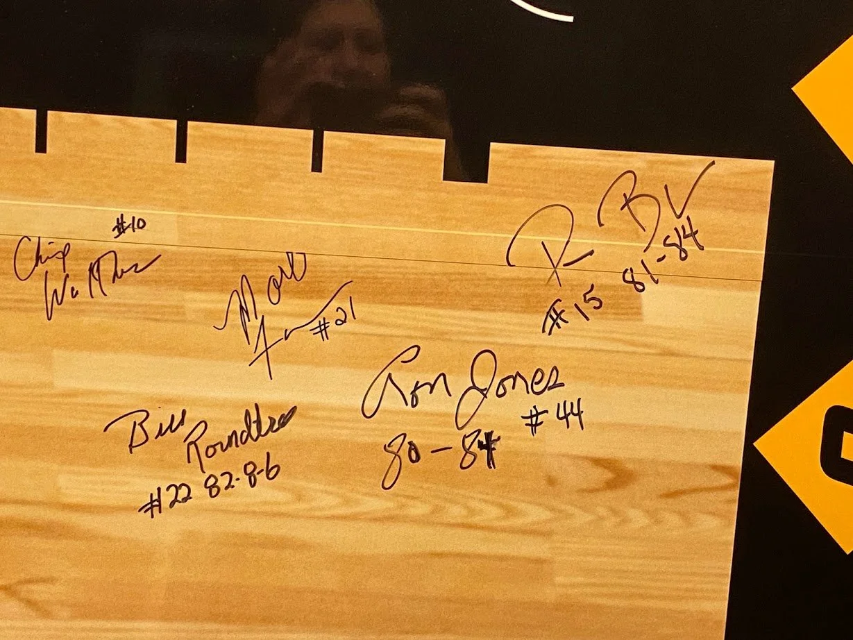 A wooden North American hockey stick with signatures and jersey numbers from various players, including Chip Wieclaw, Bill Pounders, Tom Jones, R. P. B.V, with date and number inscriptions.