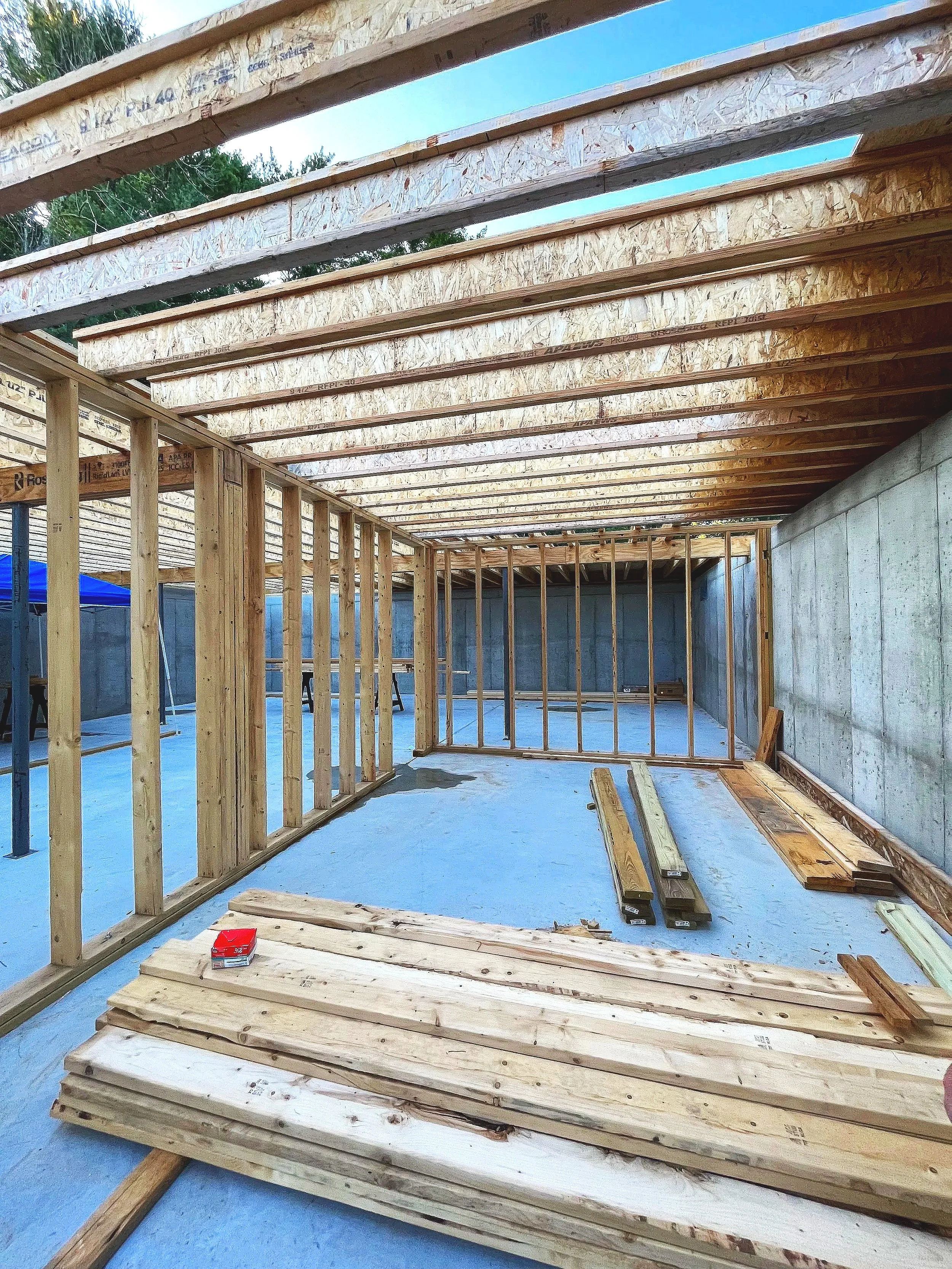 Construction site with wooden framing and a partially built ceiling, with scattered lumber on a concrete floor.