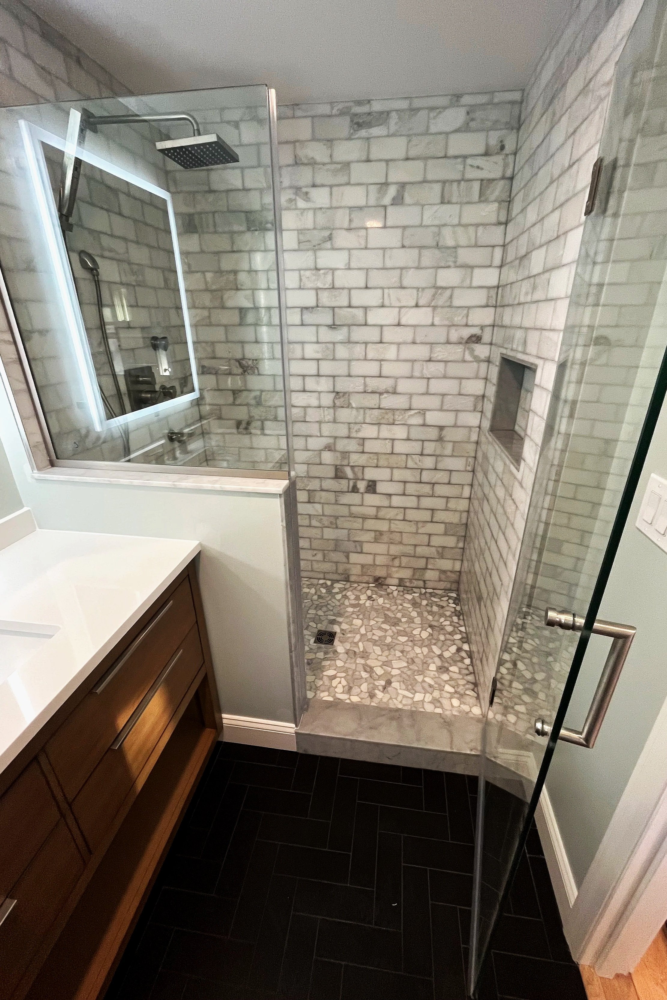 Bathroom shower with brick tile walls, a pebble floor, a small built-in niche, a rainfall showerhead, and glass walls.