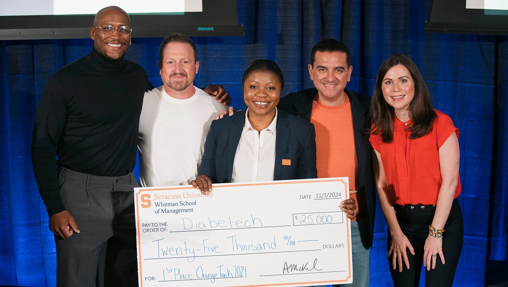 Group of five people, including CEO Stacey Tank and Cake Boss Buddy Valastro, standing together, holding a large check for twenty-five thousand dollars awarded to Diabetech. Syracuse University's Whitman School of Management.