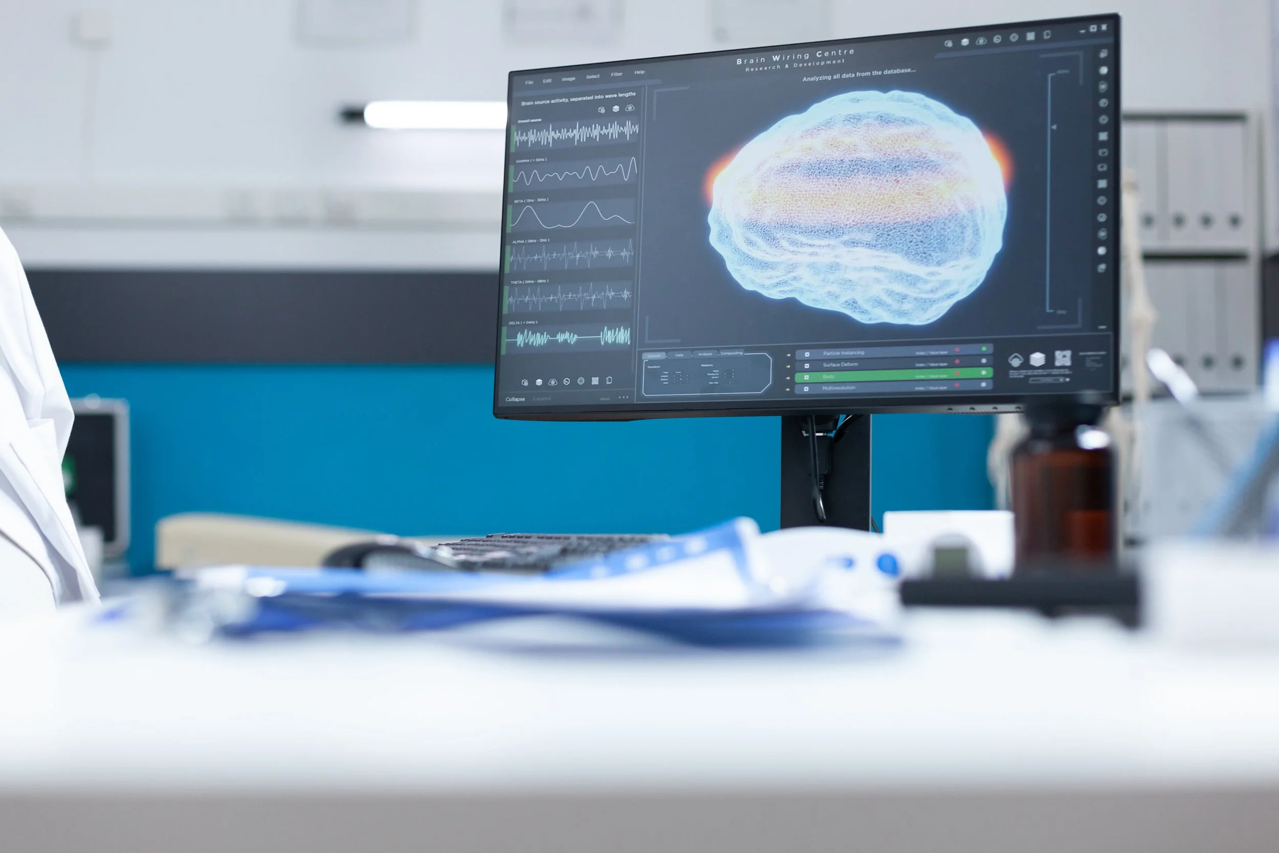 A computer screen displays a scientific visualization of a brain with data and waveforms, suggesting neural activity analysis, in a lab setting.