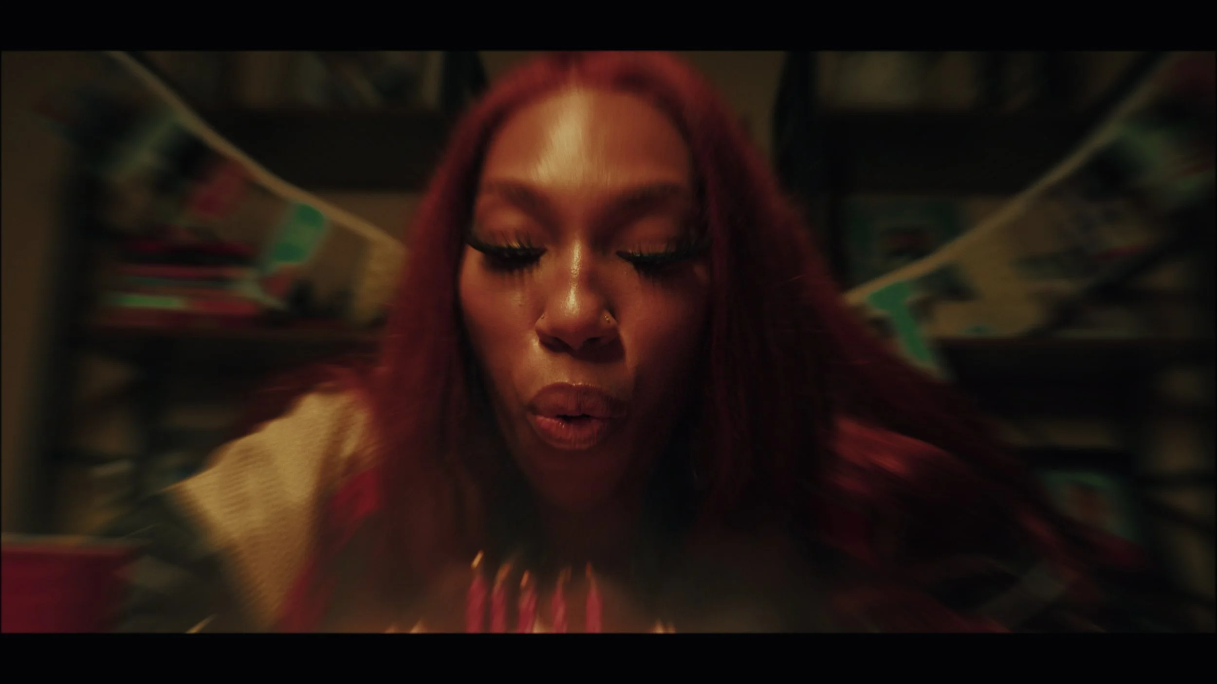Close-up of a woman with red hair and makeup, with a blurred background.