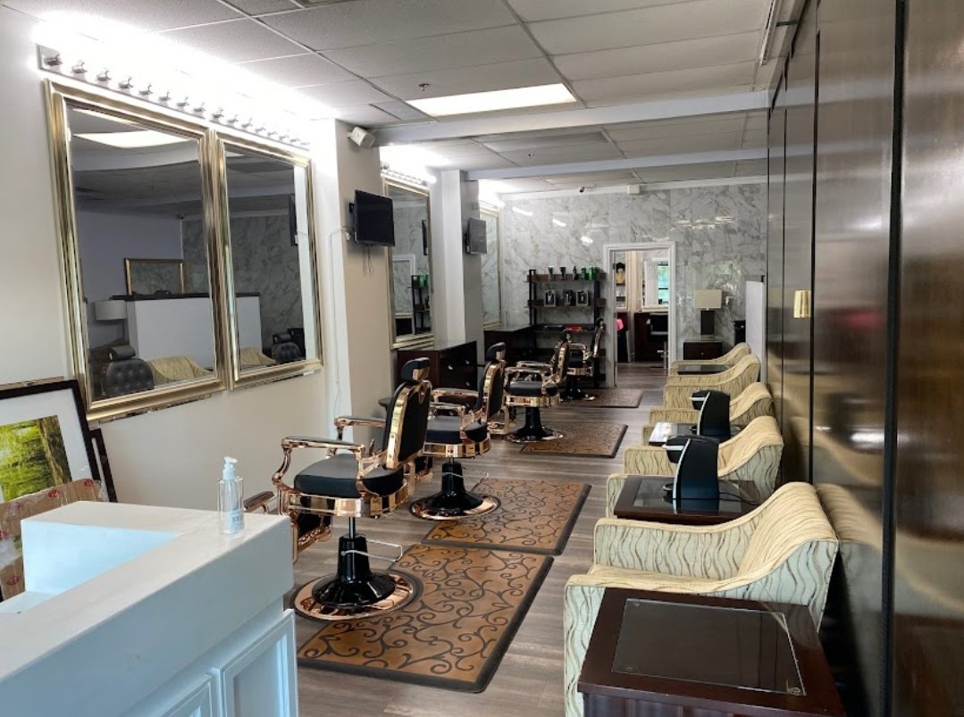 Empty hair salon with styling chairs and mirrors, front desk with hand sanitizer, and waiting area with striped armchairs.