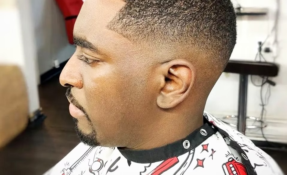 Close-up side profile of a man with a short, fade haircut in a barbershop.