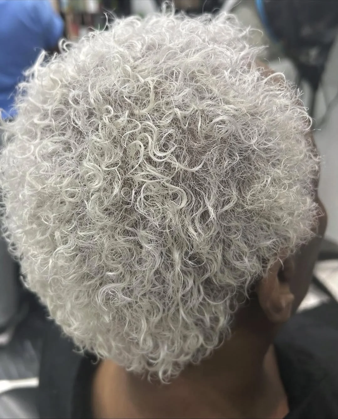 Close-up view of the top of a person's head with gray, curly hair.