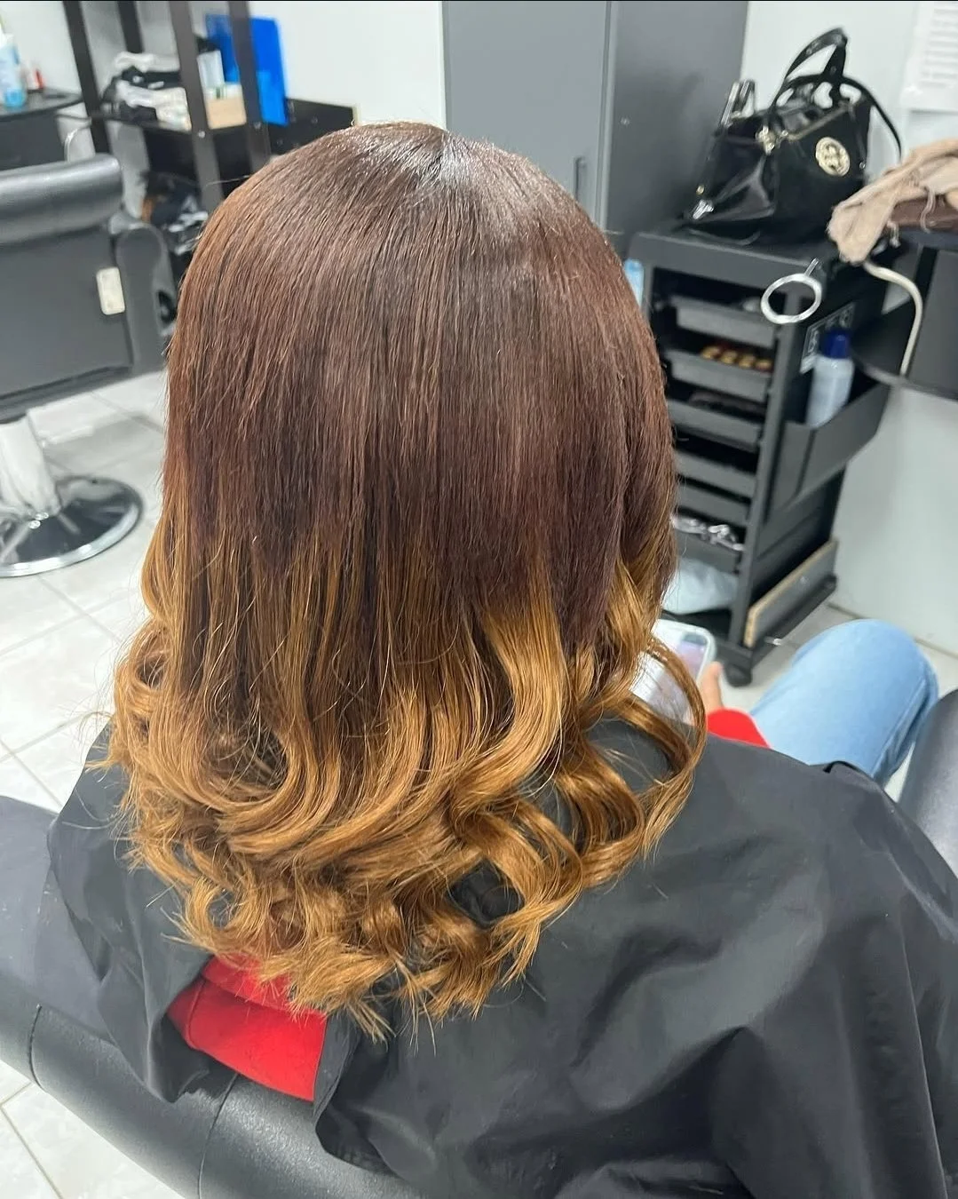 Back view of a woman at a salon with freshly styled wavy ombre hair from dark brown roots to caramel ends.