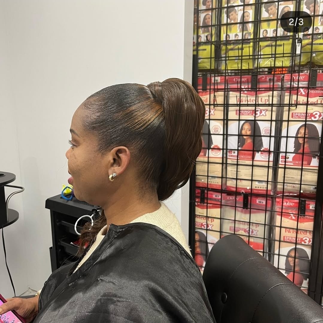 Side view of a woman with a sleek, styled updo hairstyle sitting in a salon, with hair product displays in the background.
