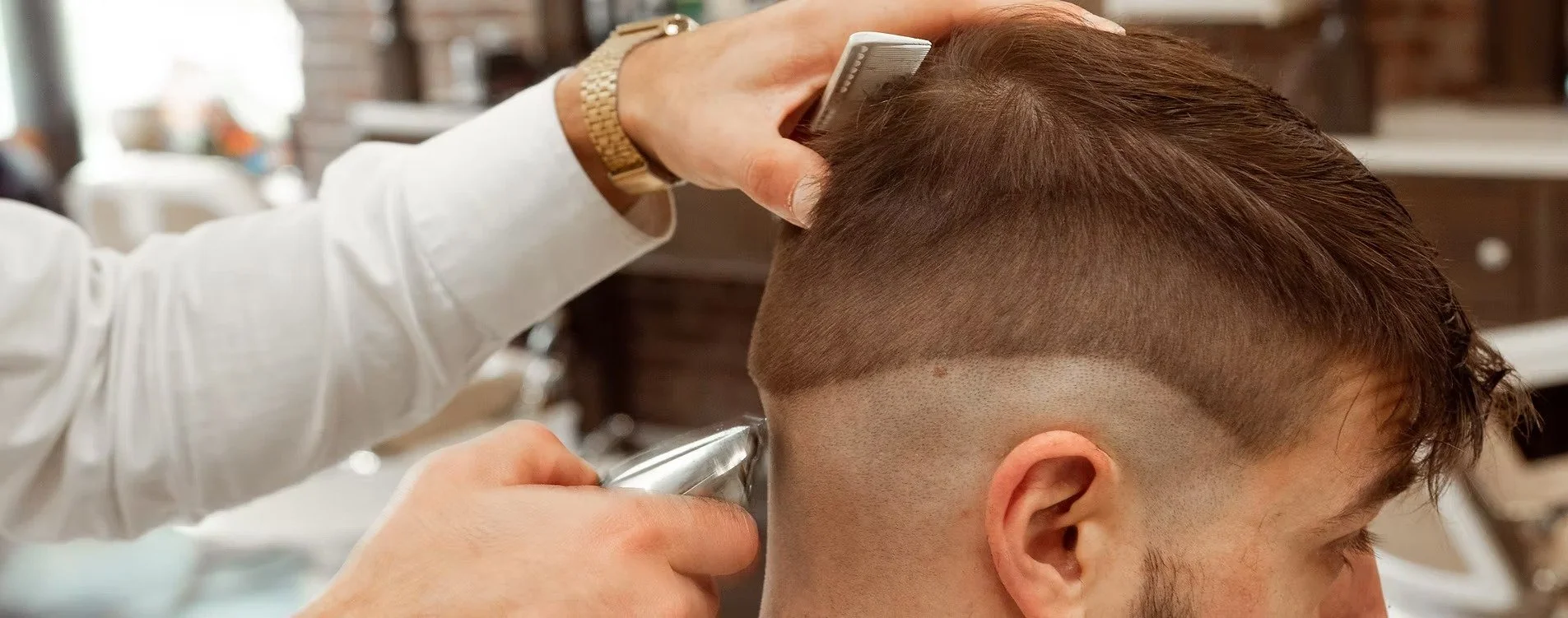 Barber trims a man's hair with electric clippers in a barbershop.