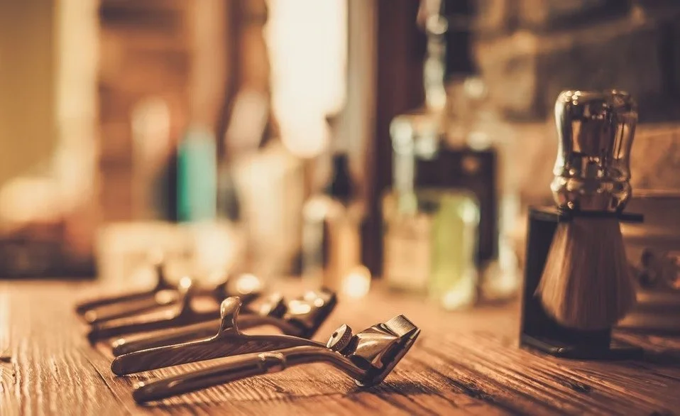A vintage safety razor and razor blades on a wooden surface in a rustic bathroom or barbershop setting.
