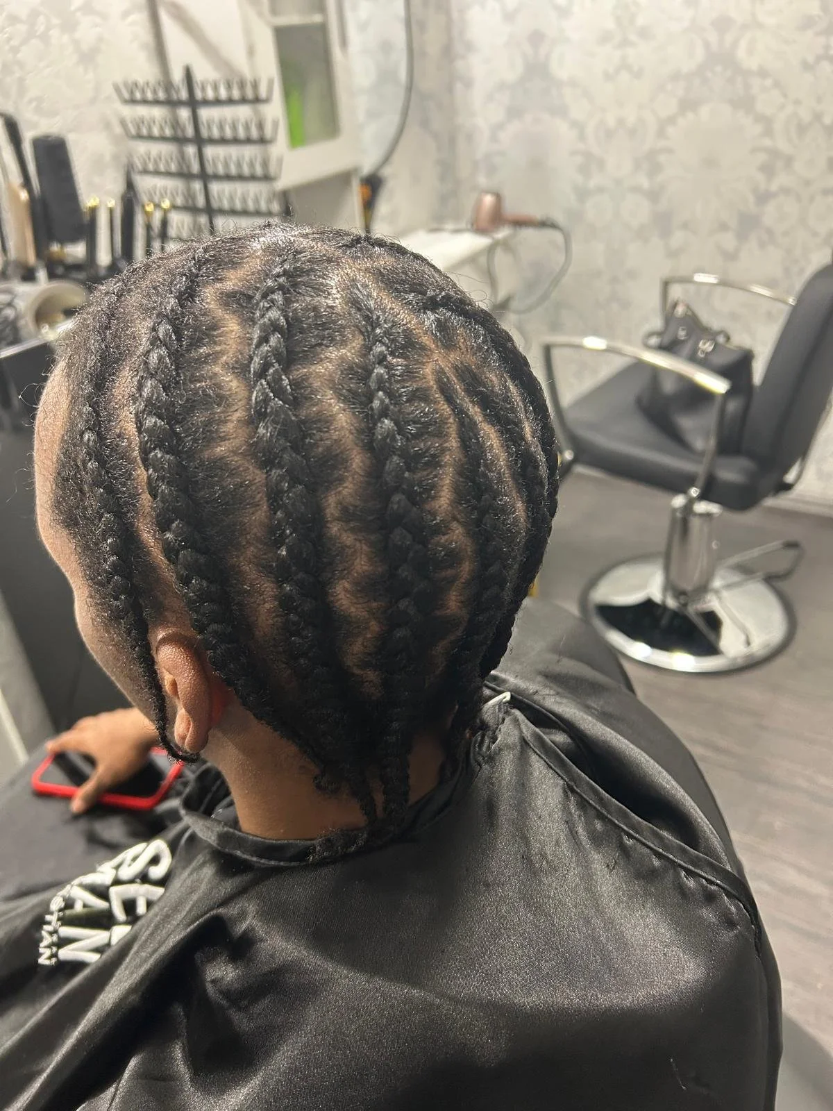 Person with freshly braided hair sitting in a salon chair in a hair salon, with styling tools and equipment in the background.