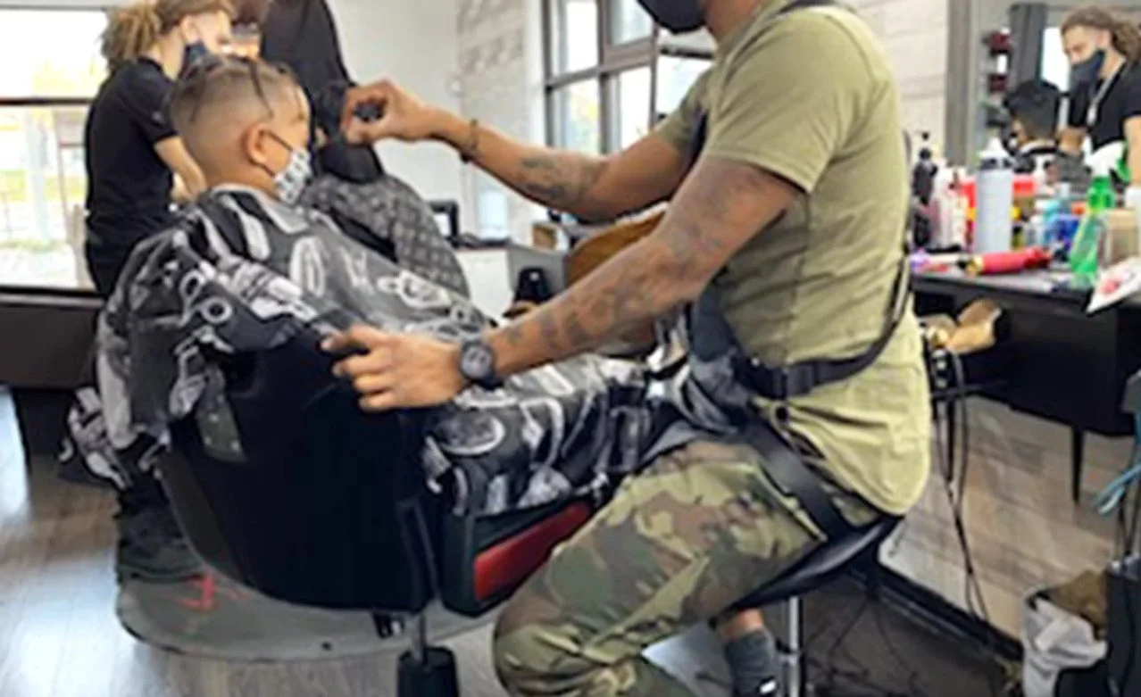 A man getting a haircut at a barbershop, with children nearby, and various hair styling tools and products on the counter.
