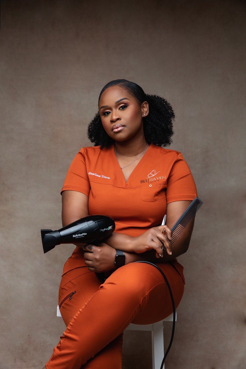 A woman in orange medical scrubs sitting on a white stool, holding a hair drying tool and a clipboard, with a neutral background.