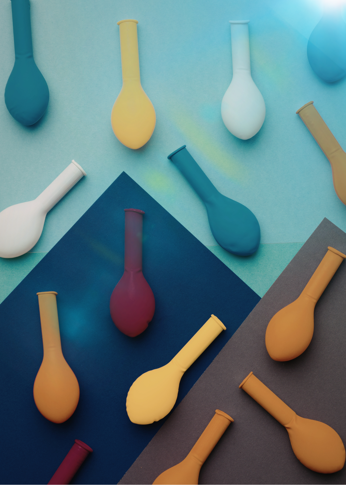 Colorful balloons arranged on a layered background of blue, gray, and dark gray paper.